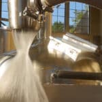 brewery equipment with white foamy liquid flowing downward amd staom;ess tank and window in background