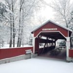 entrance to east paden red covered bridge with snow covered deciduous trees behind