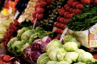 display of green and red cabbages and radishes with boxes of rows of tomatoes, eggplant, and other vegetables behind