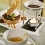 chocolate tart and chocolate sauce in warmer on white plate with tea cup and saucer in front