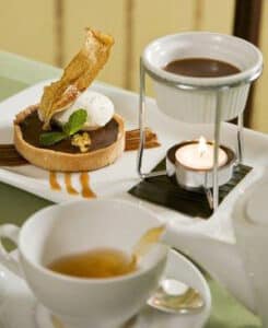 chocolate tart and chocolate sauce in warmer on white plate with tea cup and saucer in front