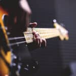 Closeup of right hand plucking and left hand fingers pressing strings on brown guitar