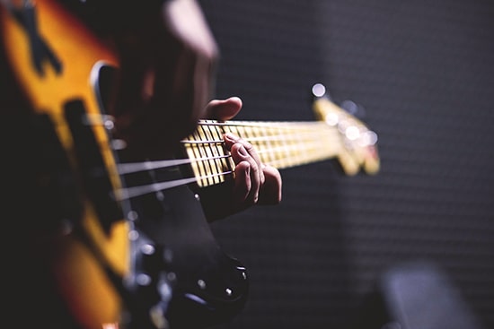 Closeup of right hand plucking and left hand fingers pressing strings on brown guitar