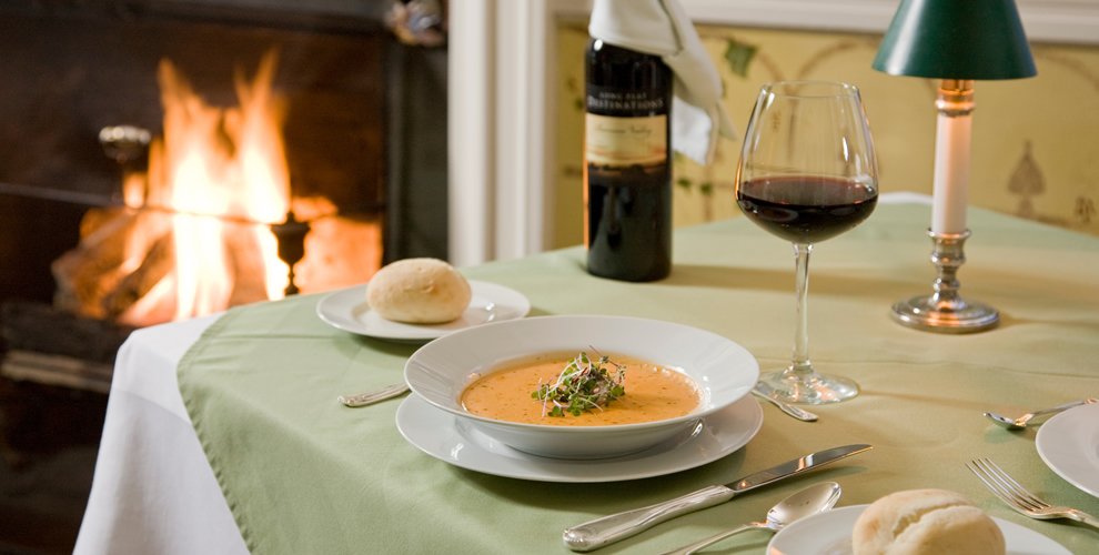 indoor dining table set for one set along fireplace, displaying delicious bowl of soup with a side of bread and wine to compliment the meal