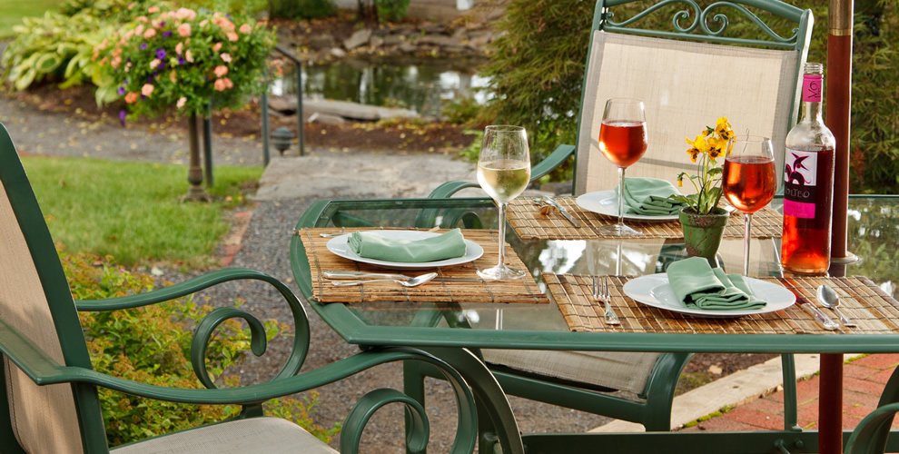 outdoor table display of green farmhouse tables with glass table top, set for 3 guests with fresh wine by the bottle poured for each glass