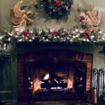 holiday decorations of two gold angels, wreath and evergreen garland with white lights on mantel