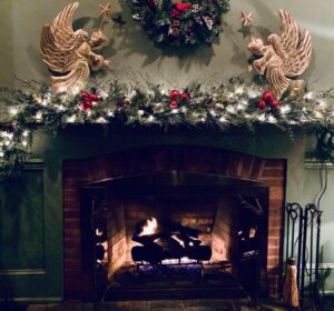 holiday decorations of two gold angels, wreath and evergreen garland with white lights on mantel