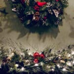 holiday decorated mantel with 2 gold angels facing central wreath, greens with white lights & red balls on mantel