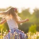 Little blonde girl spinning in a field in sunshine