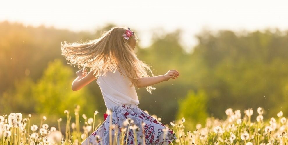 Little blonde girl spinning in a field in sunshine