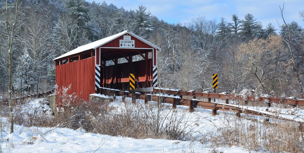Kramer covered bridge with red vertical siding surrounded by snowy landscape