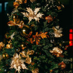 gold balls, bows, gilded leaf ornaments and tiny white lights on green Christmas tree