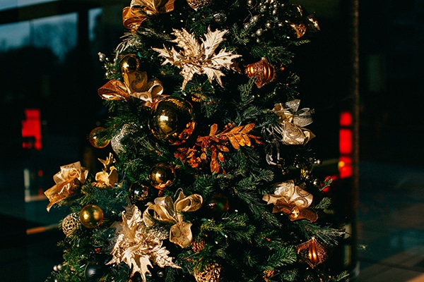 gold balls, bows, gilded leaf ornaments and tiny white lights on green Christmas tree