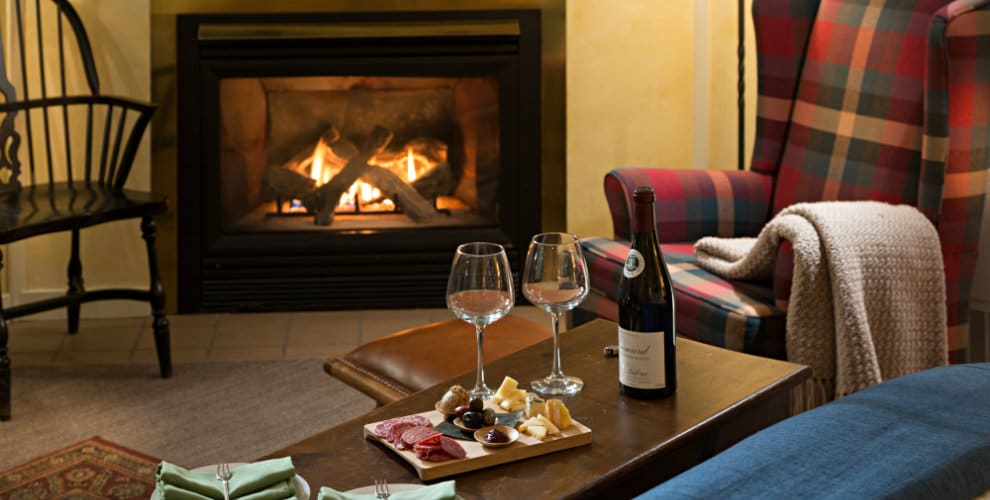 two wine glasses with board of cheese and fruit array set on coffee table in front of fireplace