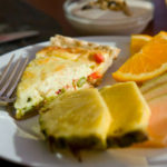 vegetable quiche with 2 semicircular orange slices and 2 pineapple slices with rind on white plate