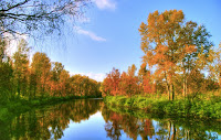down the river in autumn during sunset with blue skies and colors of leaves changing along the river banks