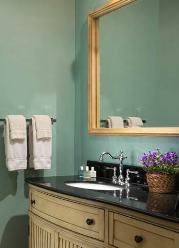 vanity with black countertops and large mirror with display of purple flowers in basket