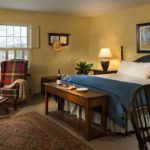 Inn room with fireplace wingchair king bed with blue & white bedding chair desk