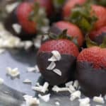 5 chocolate dipped strawberries on glass plate with white chocolate shavings scattered over them