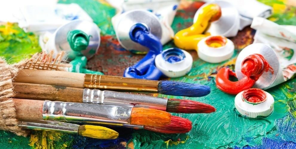 Tubes of brightly colors paint and artist paint brushes on painted canvas