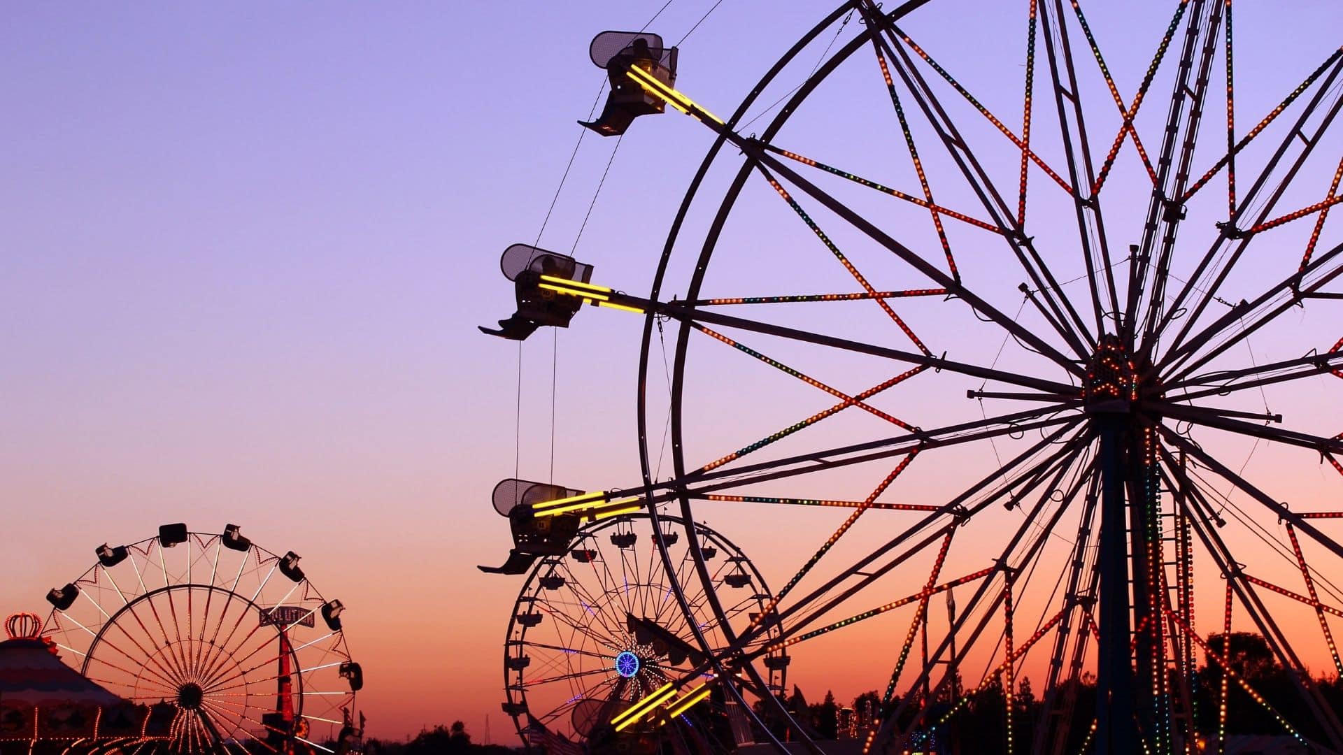 multiple ferris wheels at a state fair with purple and rose sunset background