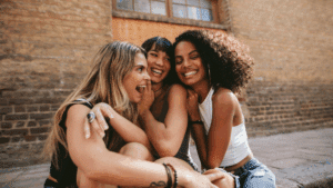 three young women sitting together outdoors laughing and smiling