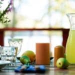 Outdoor dining table set with several place settings, fruit, candles, and juice