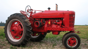 vintage red tractor parked in a grassy field under an open sky