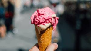hand holding a waffle cone with scoops of strawberry and vanilla ice cream 