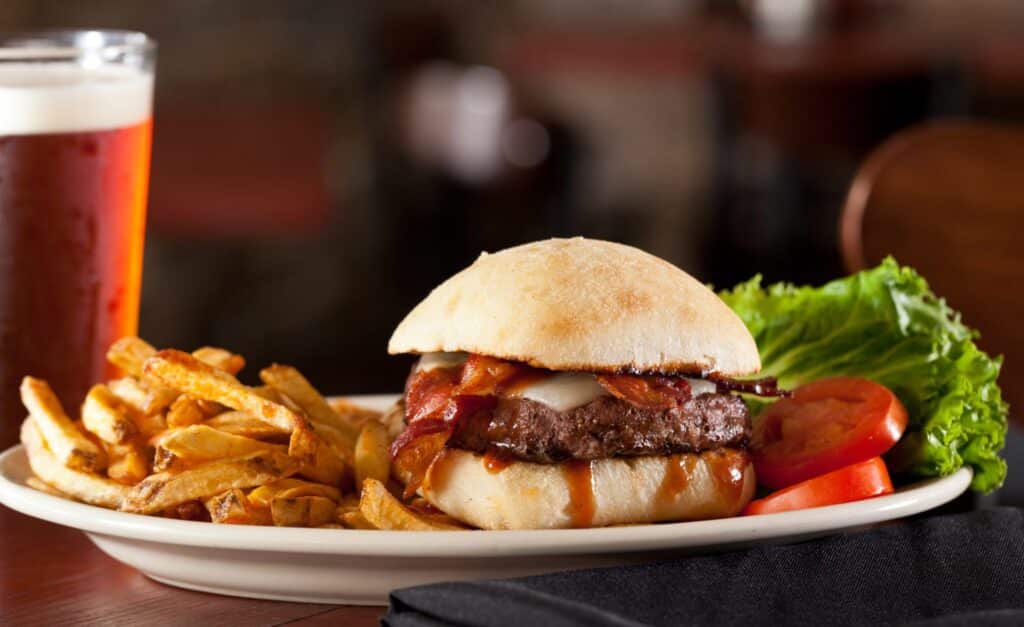 closeup of glass of beer white plate with fries burger lettuce tomato