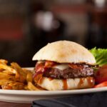 closeup of glass of beer white plate with fries burger lettuce tomato