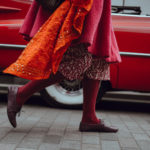 legs of woman wearing swirling red dress and tightswalking in front of red car